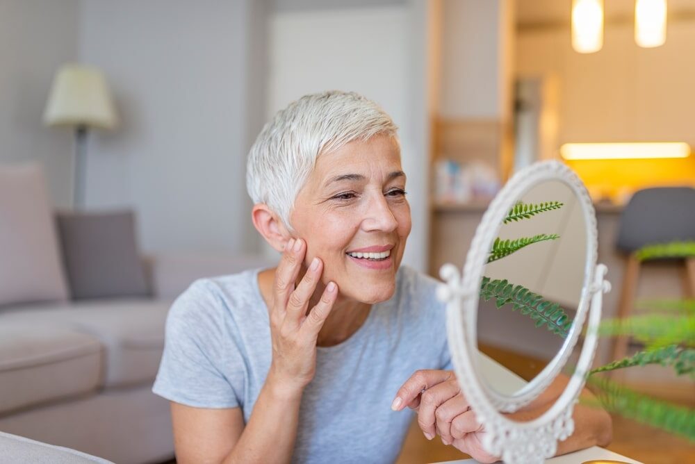 Smiling adult lady looking at herself in mirror